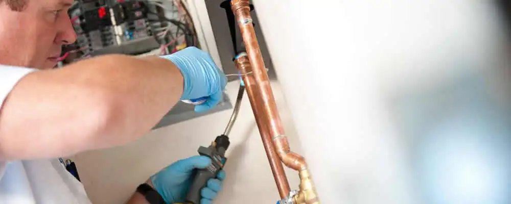 Water heater repair technician testing copper pipe connections and controls in Fort Worth, TX